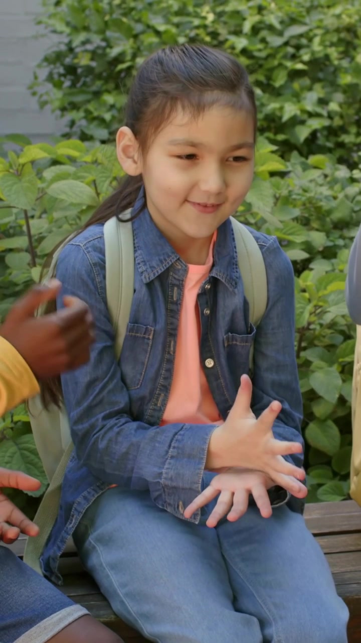 Video vertikal: Anak laki-laki bermain meraih dan anak perempuan bermain permainan tangan mengenakan jaket denim di bangku, terlihat ransel.