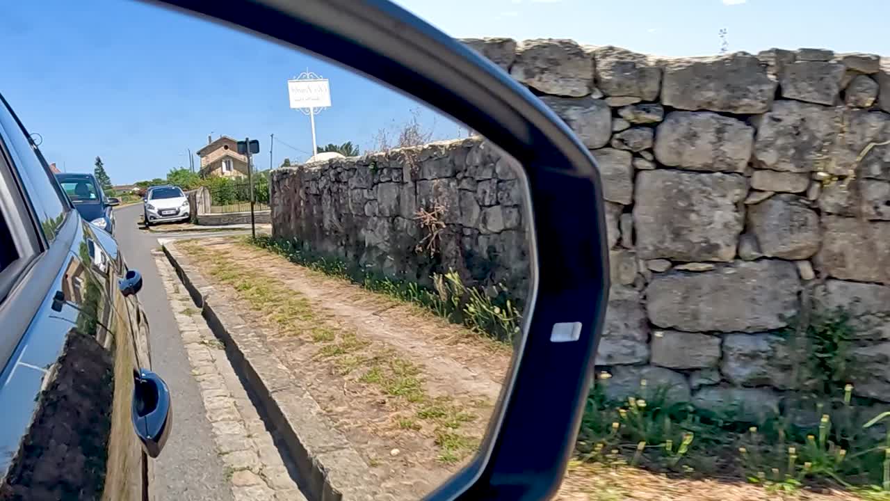 Close-up view of a vehicle's side mirror reflecting a rural road and stone wall