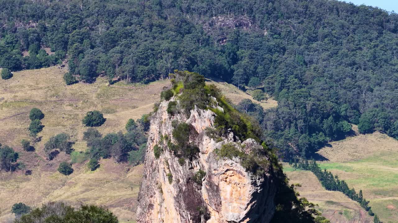 Drone footage capturing Nimbin Rocks' rhyolite formations surrounded by eucalyptus forest under clear daylight