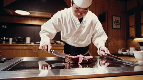 professional chef slicing cooked meat on a teppanyaki grill