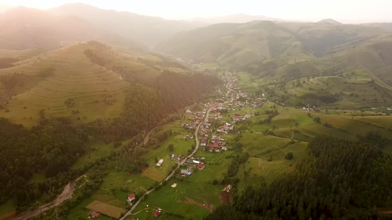 drone captura un pueblo encantador que se extiende a través de un valle verde exuberante rodeado de colinas bajo el cálido resplandor del sol de la tarde