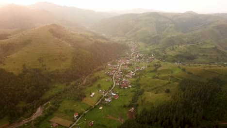 drone captura un pueblo encantador que se extiende a través de un valle verde exuberante rodeado de colinas bajo el cálido resplandor del sol de la tarde