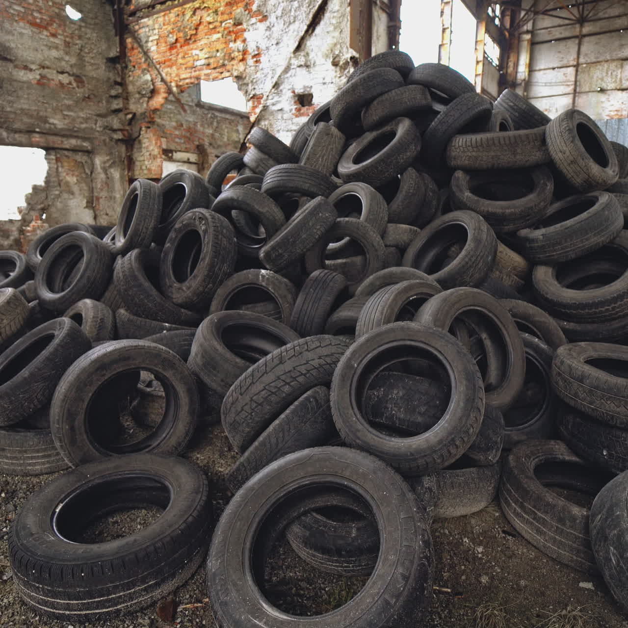 Landfill of used automobile tires on the old abandoned plant inside. Huge piles of black waste wheels from different vehicles. Motion bottom up