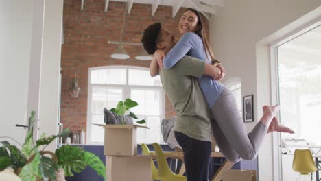 happy biracial couple moving house, embracing and smiling in kitchen