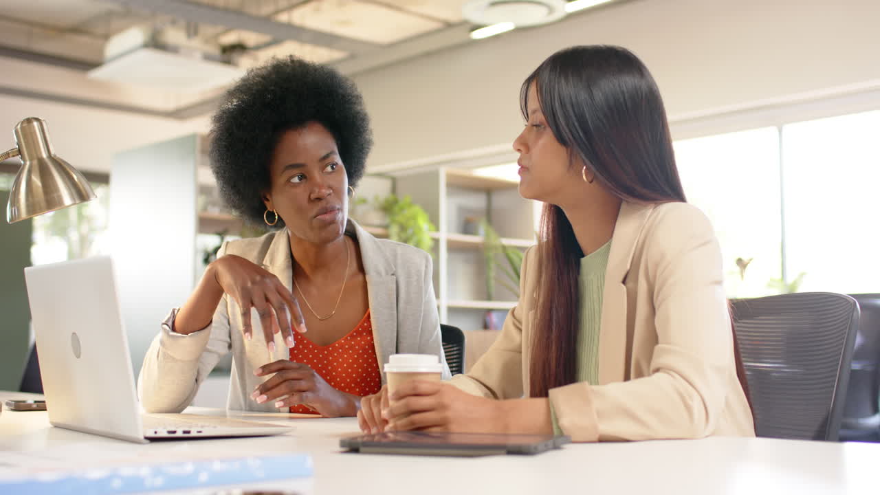 Diverse female creative colleagues in discussion using laptop in office, slow motion