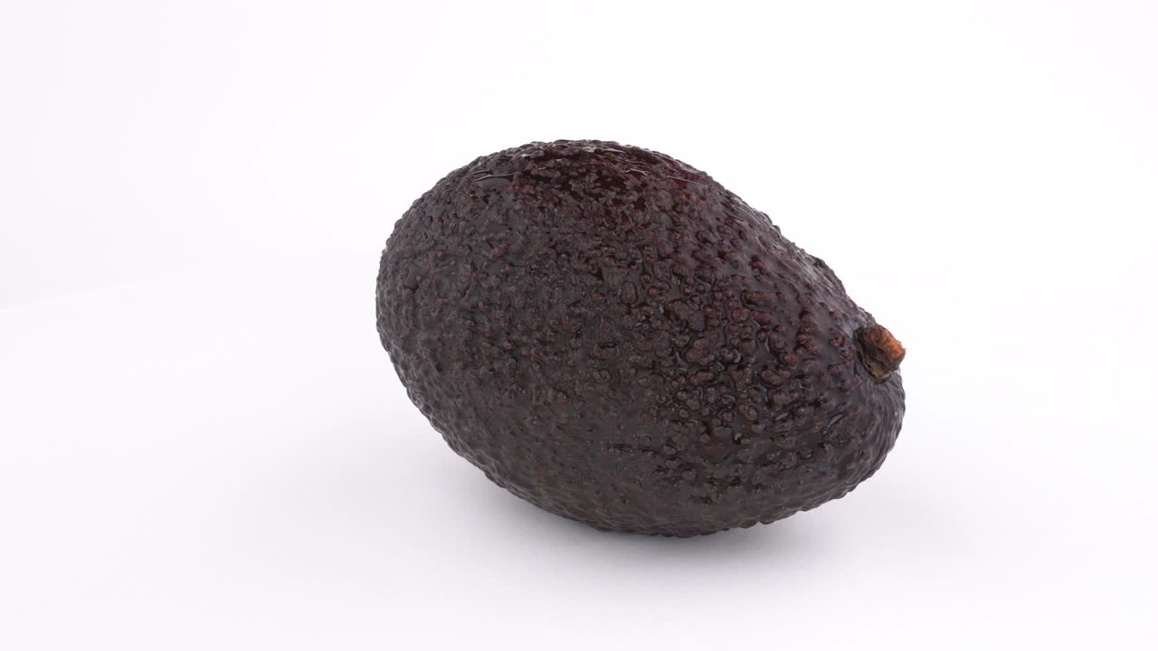 Avocado Haas crudo ruota lentamente su un piatto girevole. Isolato su sfondo bianco. Macro ravvicinata.