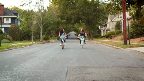 two teen girls riding bikes in a quiet street, front view