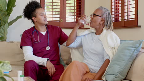 caregiver handing glass of water to senior woman at home, sharing smile