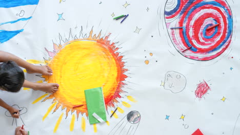 children drawing a solar system on a large sheet of paper