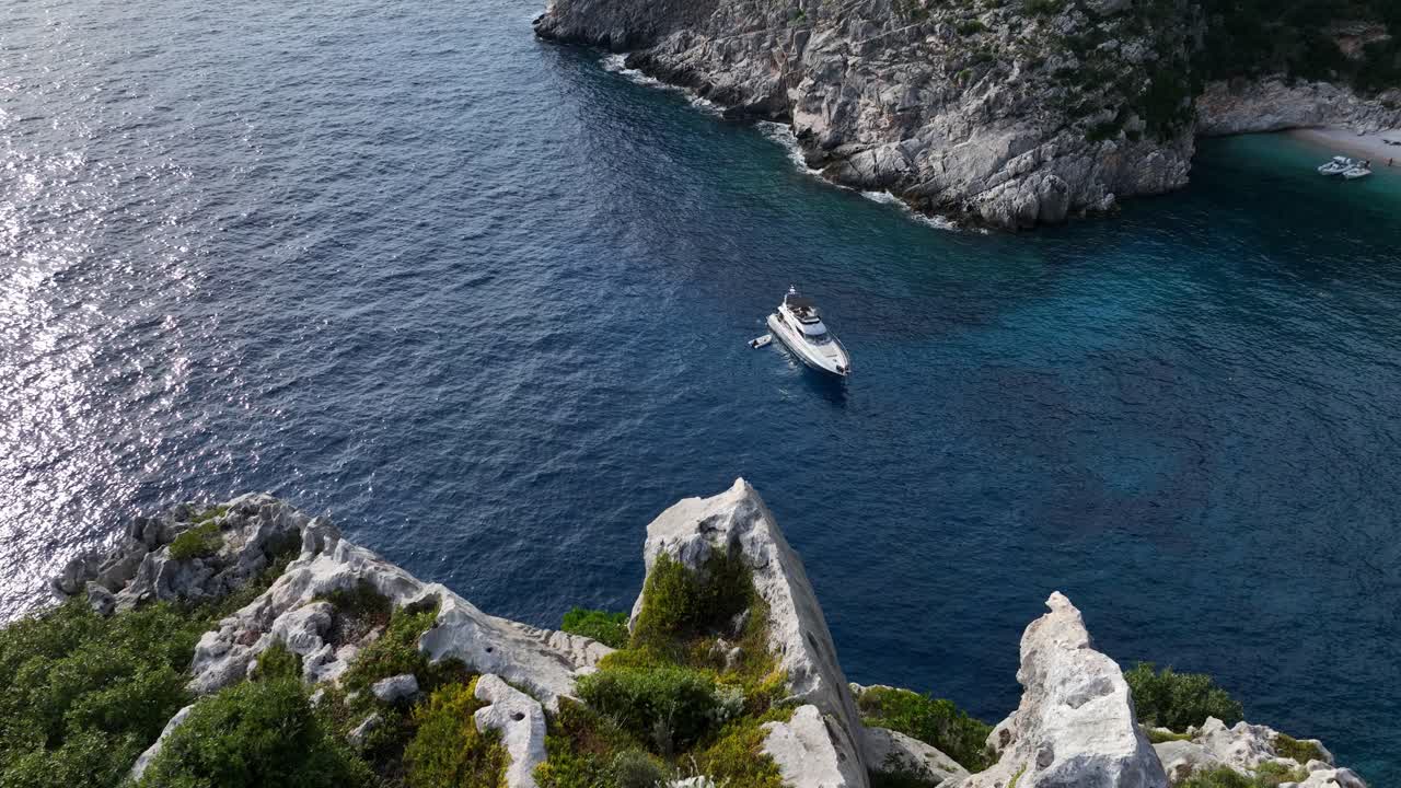 Aerial reveal of yacht in sparkling ocean near rugged coast and cliffs in Shpella, Albania at golden hour