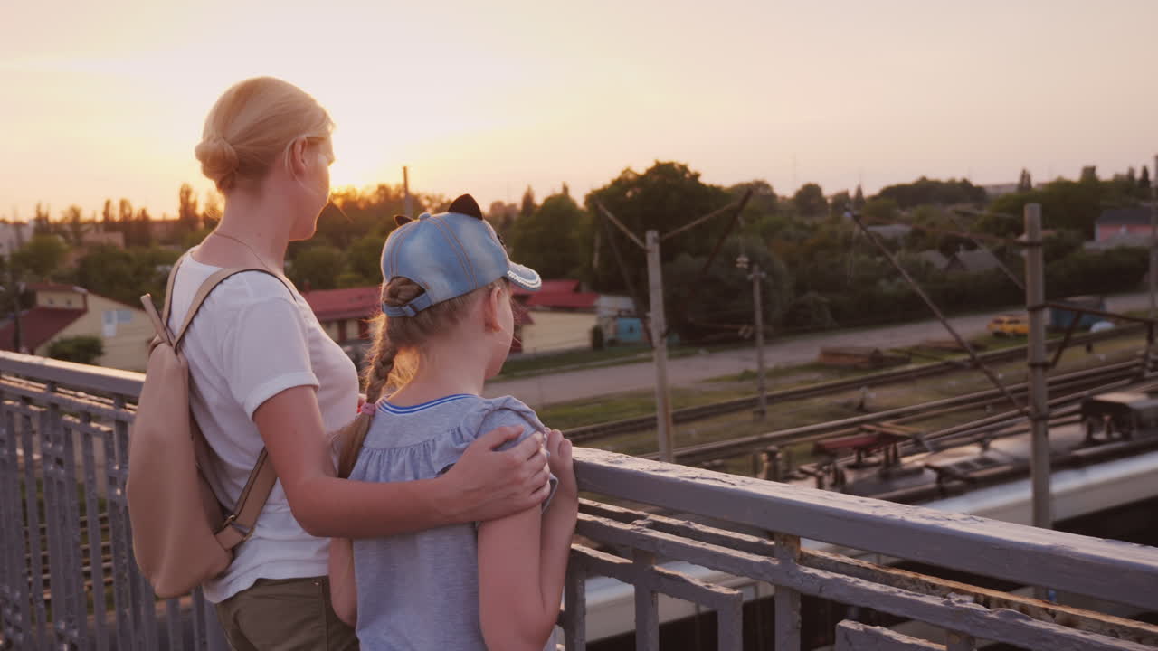 한 여자와 그녀의 딸이 다리 위에 서서 아래의 기차를 본다