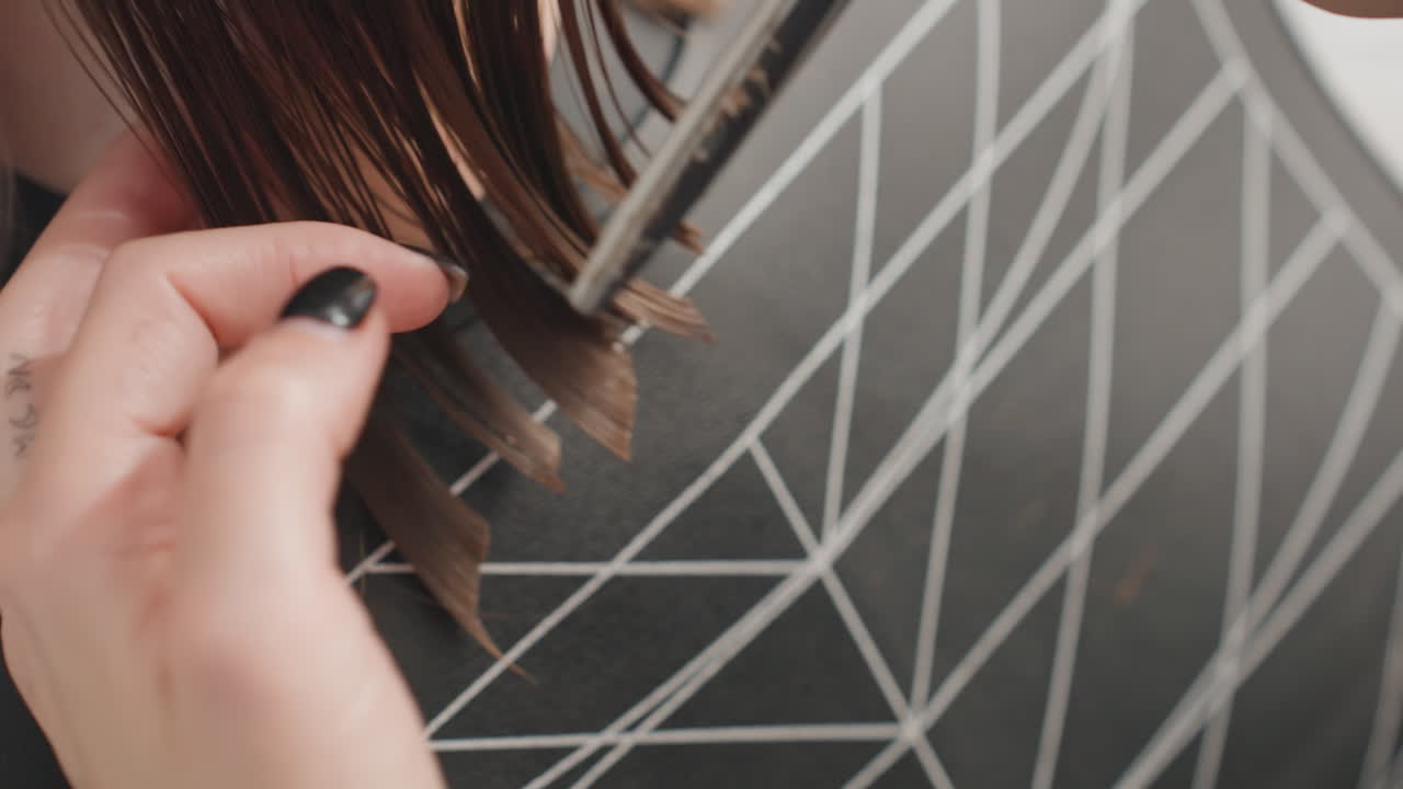 closeup stylist trimming straight brown hair with comb and shears senior hairdresser performs precise horizontal cut on client ends, geometric cape backdrop, steady hands with black nails, modern