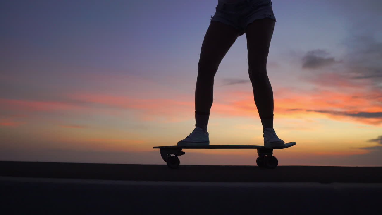 hermosa chica monta una patineta en la carretera contra el cielo al atardecer.