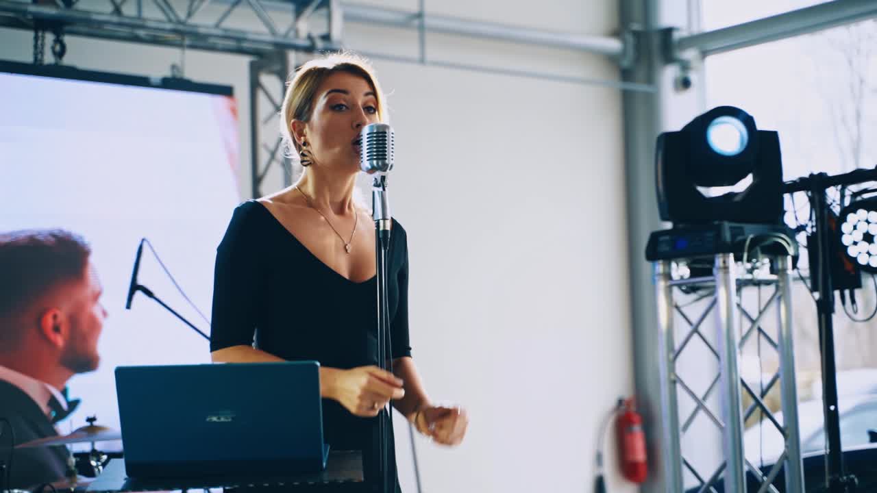 Beautiful woman singing into the mic. Young female singer in black dress on the background of wedding video clip on stage.
