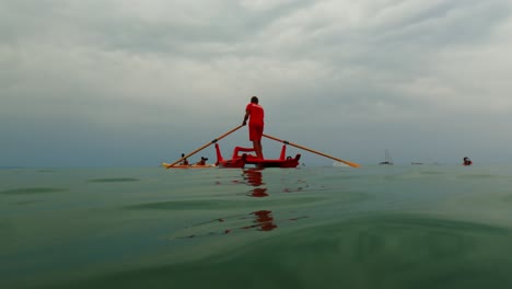 red italian lifeguard ready for first aid emergency standing and rowing rescue boat while watching people on kayak and sup in background