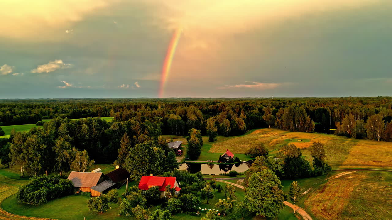 arco iris sobre el campo con el dosel de los árboles, el bosque y las casas de la aldea, el lapso de tiempo