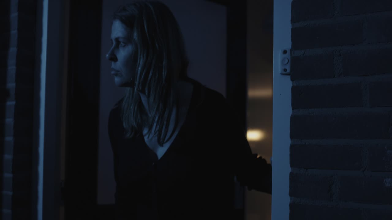 mujer preocupada abriendo la puerta principal de su casa y mirando a su alrededor por la noche