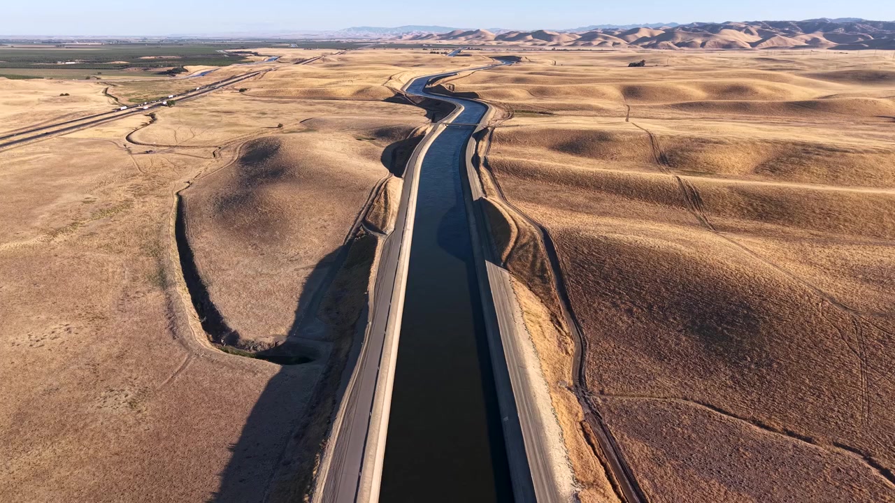 Acqua che scorre attraverso i canali fluviali dell'Acquedotto della California. Ampio paesaggio di un fiume artificiale agricolo che fornisce acqua a terreni agricoli per l'irrigazione in zone rurali lungo l'autostrada I-5.