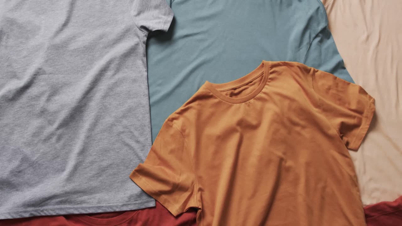 Video of flat lay of multi coloured t shirts with copy space on white background