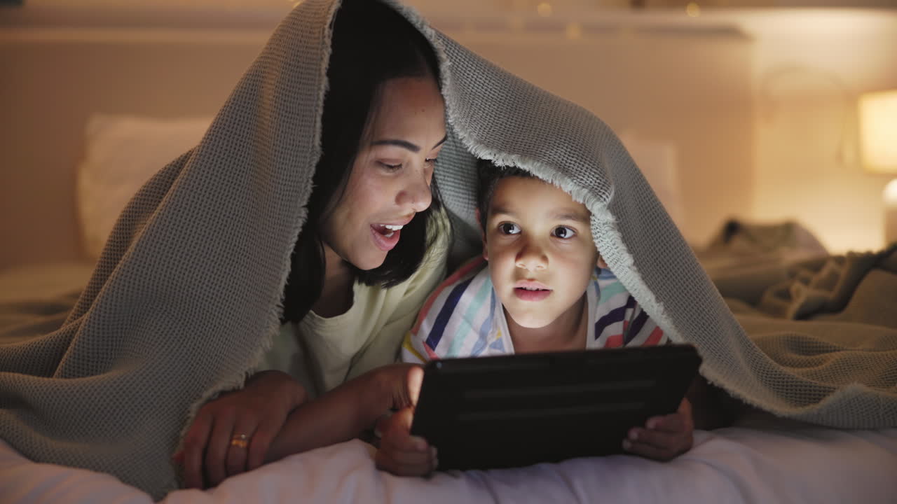 Mother and son enjoying tablet time under a blanket