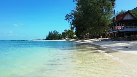 Calm-clear-water-of-turquoise-lagoon-washing-white-sand,-beach-bar-on-shore-of-tropical-island-in-Thailand