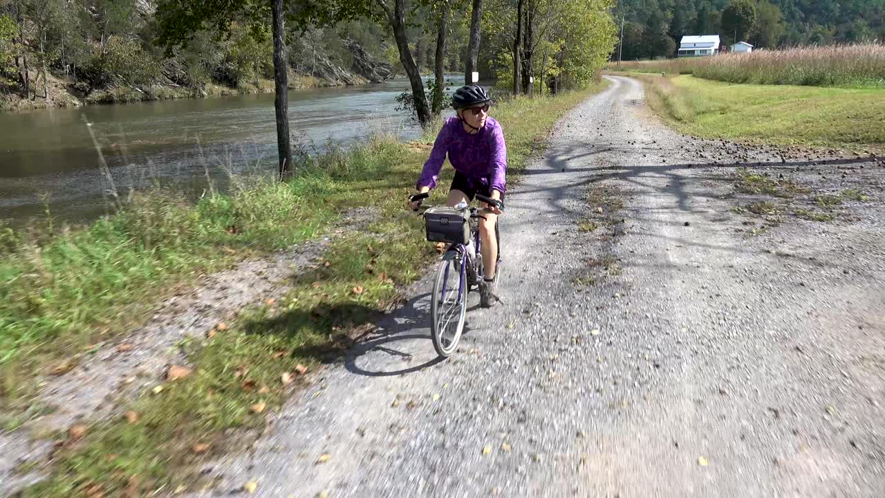 mujer bonita y madura en una bicicleta de montaña montando en un camino de grava con un río a un lado y tierras de cultivo al otro