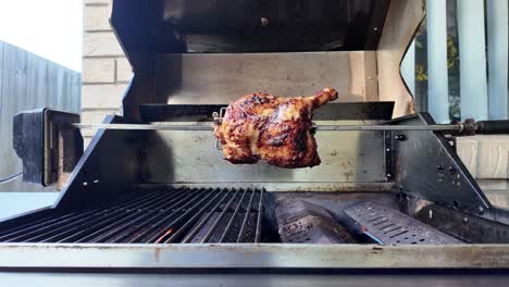 opening of a bbq hood to reveal a chicken being grilled on a rotisserie