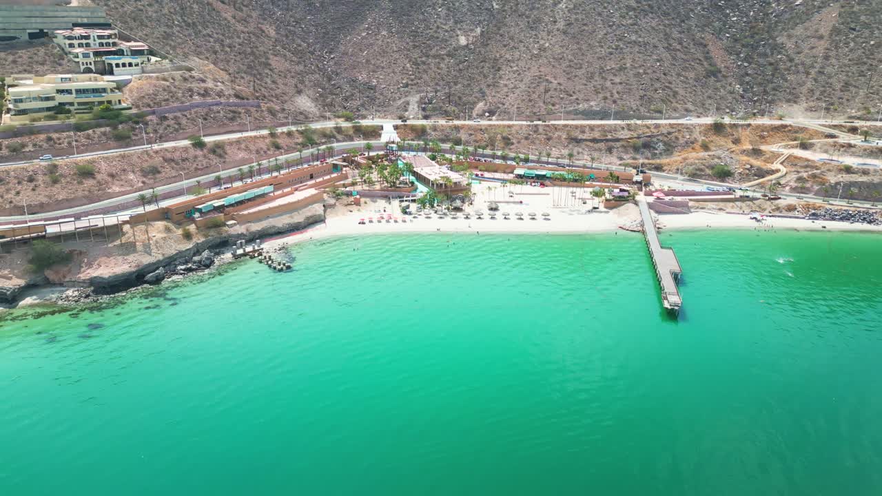 Beautiful aerial shot of Playa Coromuel in La Paz, showcasing the clear turquoise waters and peaceful beach scene with a pier stretching into the ocean