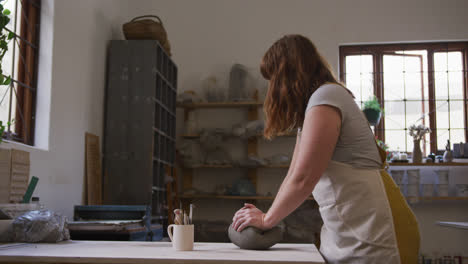 female potter wearing face mask and apron kneading the clay at pottery studio