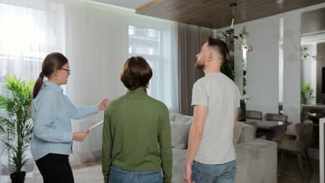 backview of woman professional real estate agent make a apartment tour shows modern design for a young family couple. home buying concept.