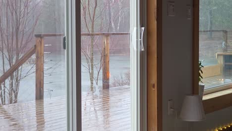 fireplace reflects in cabin window as rain falls on terrace by forest lake