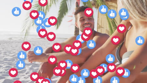 heart and like icons floating against caucasian couple talking while sitting on the beach
