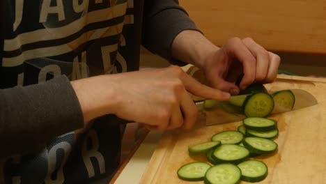 a young man cuts a cucumber with a knife for a salad