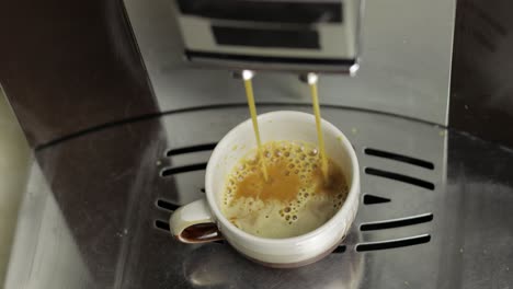 Espresso-shot-pouring-out-from-coffee-machine-in-small-white-and-brown-cup.-Close-up-footage