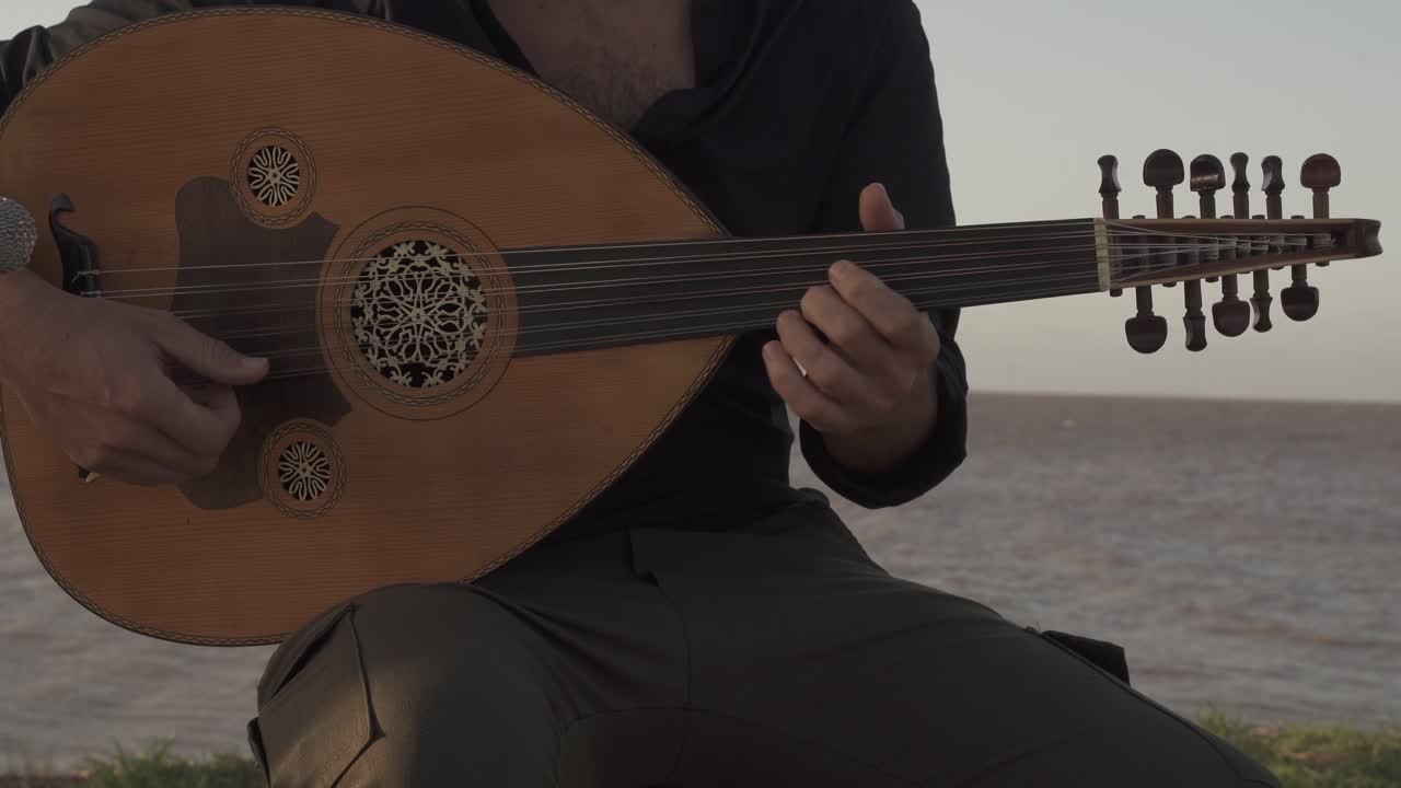 una grabación de mano de un músico masculino mientras toca en vivo usando su instrumento musical de cuerda llamado "oad