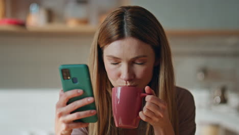 lady cellphone drinking coffee at kitchen close up. portrait woman browsing