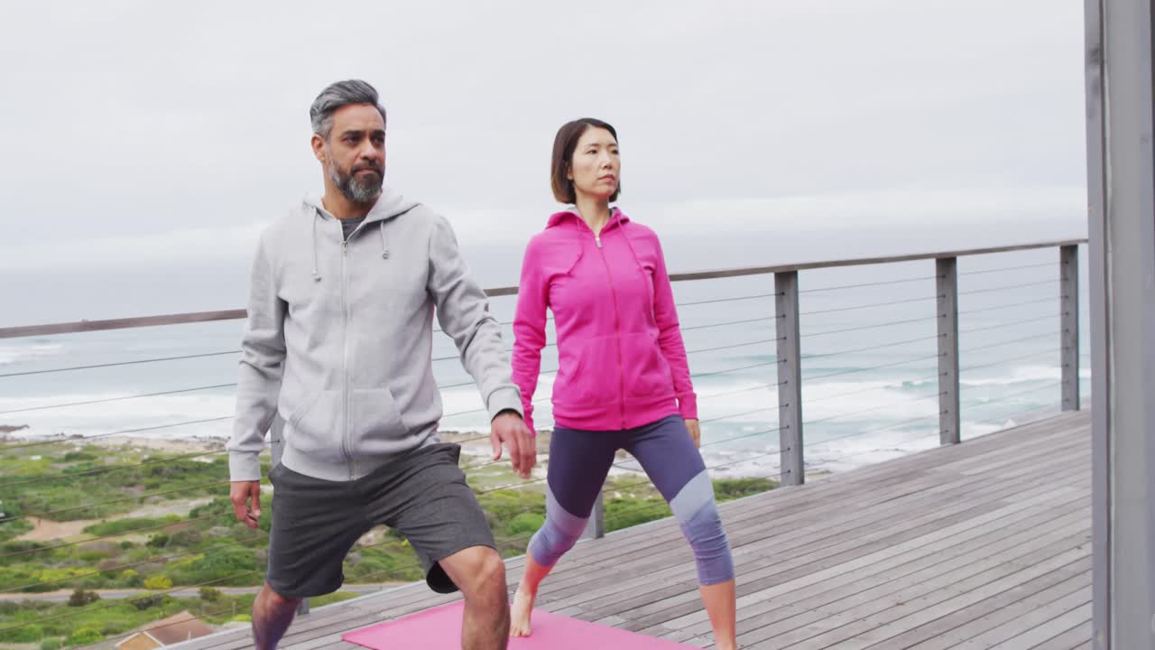 pareja feliz diversa haciendo yoga, de pie y estirándose en el balcón
