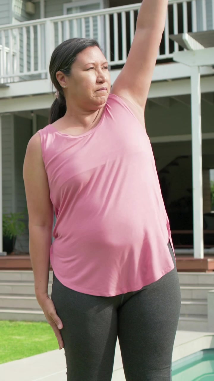 Video verticale: Donna in canotta rosa che inizia a fare oscillazioni delle braccia per stretching a bordo piscina, con smartwatch.