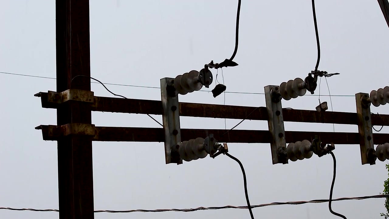 Silueta de poste eléctrico, aisladores cerámicos y líneas aéreas contra un cielo monzónico nublado — para proyectos de metraje B de energía, servicios públicos, infraestructura y clima.