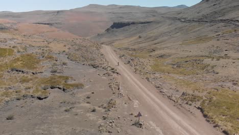 aerial shot following a mountain biker climbing up a pass on a gravel road