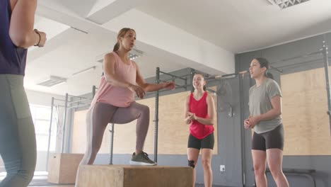 unaltered diverse women motivating determined woman jumping on boxes at fitness class, slow motion