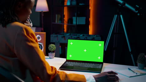 Young woman using laptop with isolated greenscreen display at her home office