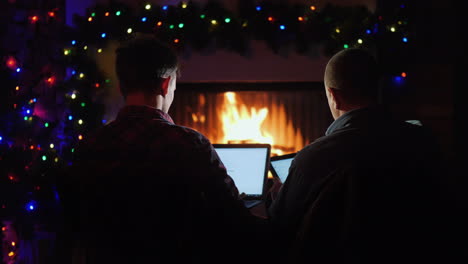 father and son use laptop and tablet order christmas gifts while sitting by the fireplace