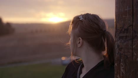 over the shoulder view of a young girl with flowing hair in a braid, looking at a romantic and peaceful sunset in nature