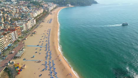 aerial-views-in-the-morning-on-the-beach-of-Lloret-De-Mar-on-the-Costa-Brava-of-Gerona,-passenger-boat,-few-people-on-the-beach