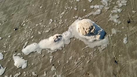 Espuma-De-Playa-Sucia-Que-Se-Mueve-Lentamente-A-Través-De-La-Arena-Galesa-Con-Olas-De-Marea