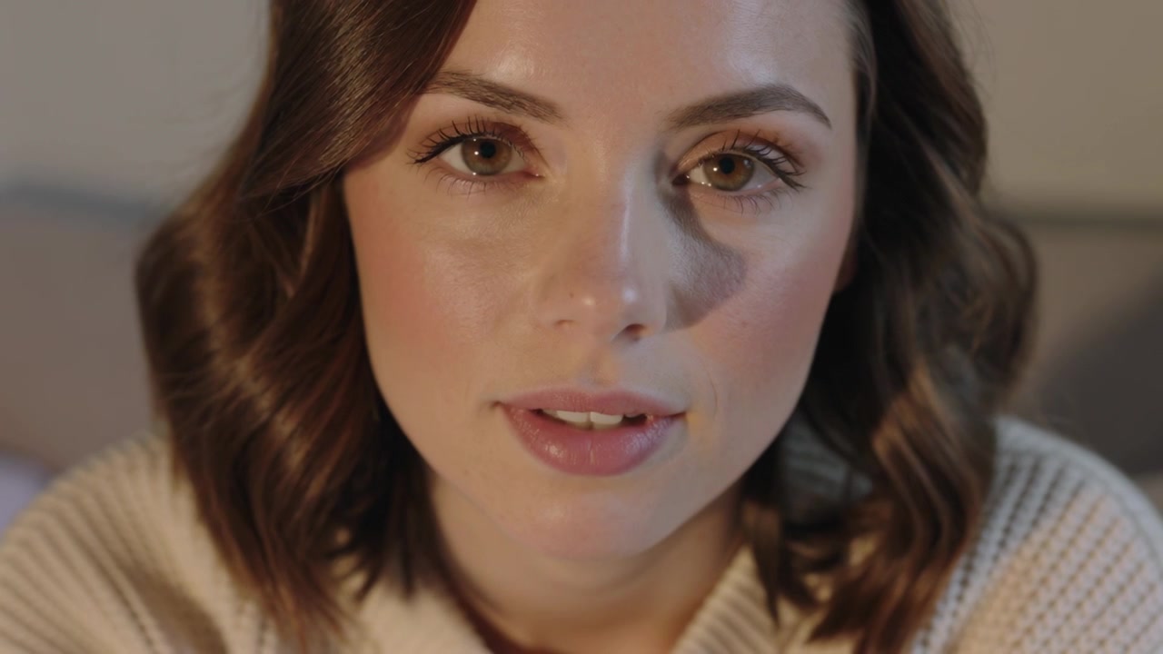 Recording starting woman holding gaze, blinking and parting lips at bedroom in cream sweater