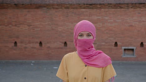 woman in pink hijab in front of brick wall