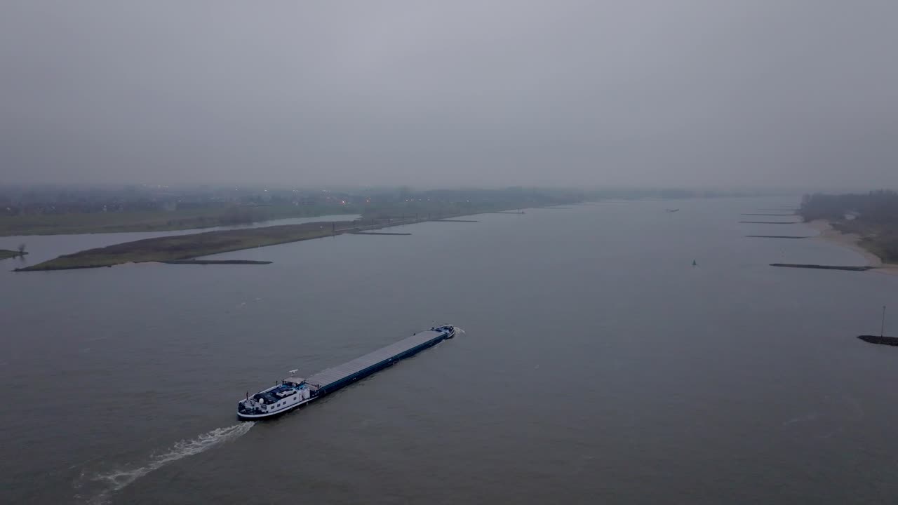 Follow drone shot A Cargo ship on the Waal river during foggy conditions