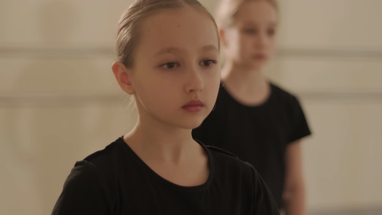 группа молодых студентов балета в черной танцевальной одежде практикует позиции в просторной балетной студии с деревянным полом и настенными решетками. сосредоточенные выражения и синхронизированные движения.